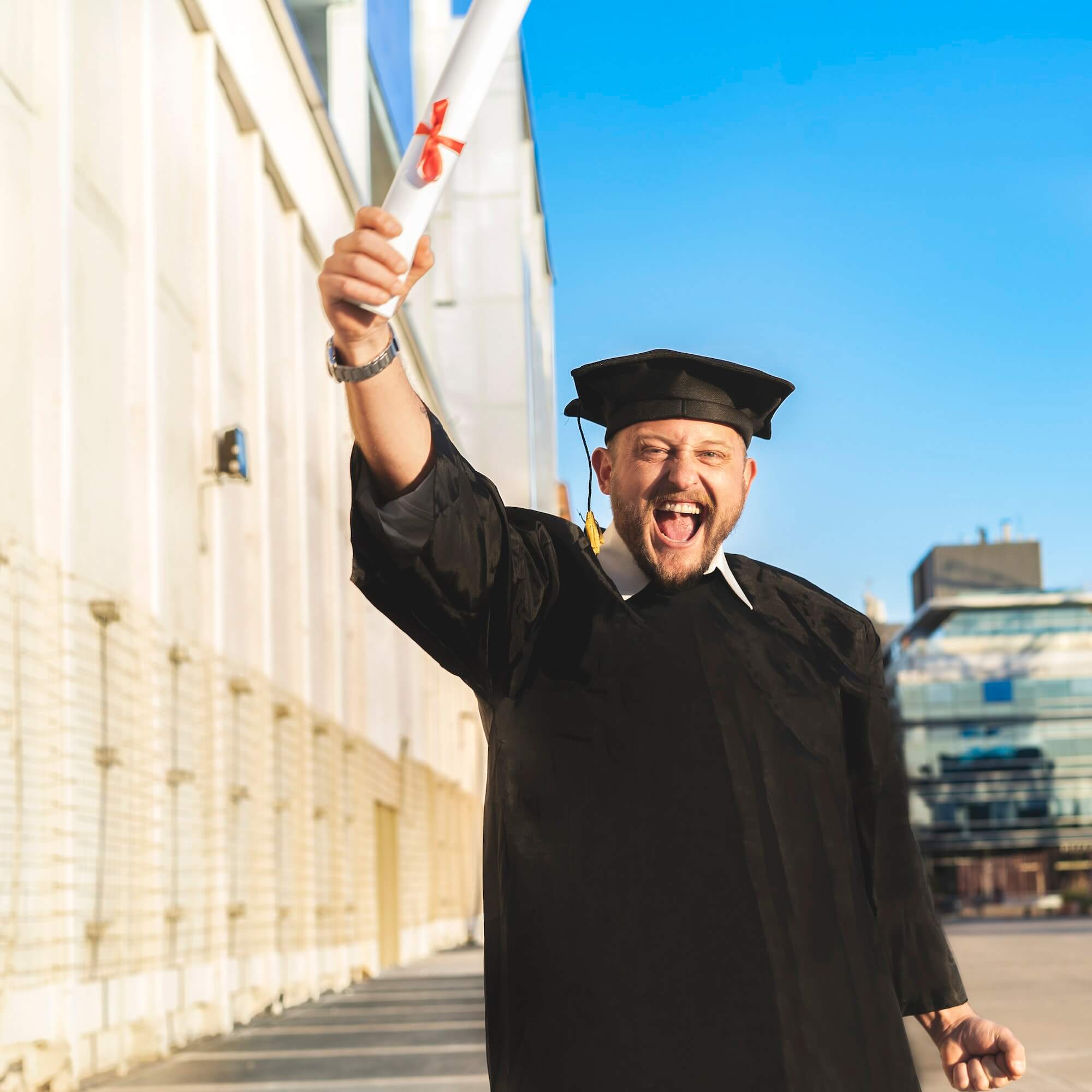 Happy graduated adult man wearing a bachelor gown and a black mortarboard